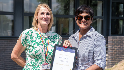 Two people standing in front of a building with large windows; one holding a framed certificate